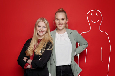 Pia Petersen und Lara Schomaker vor einer roten Wand. Rechts neben ihnen ist sein Männchen in weiß auf die Wand gemalt.