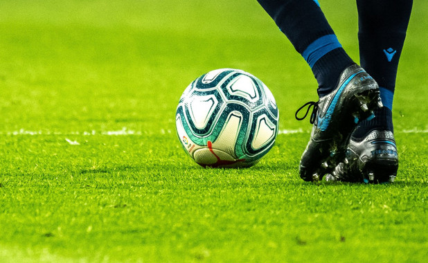 Ein Fußball auf einem Fußballfeld. Daneben die Beine einer Fußballspielerin.