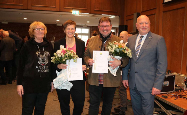 Britta Satzy auf einem Gruppenfoto mit drei weiteren Personen. Sie und eine weitere Person halten ein Dokument und Blumen in den Händen.