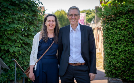 Stephan Röhr und seine Frau in Abendkleidung in einem Durchgang zwischen zwei hohen gepflegten Hecken.