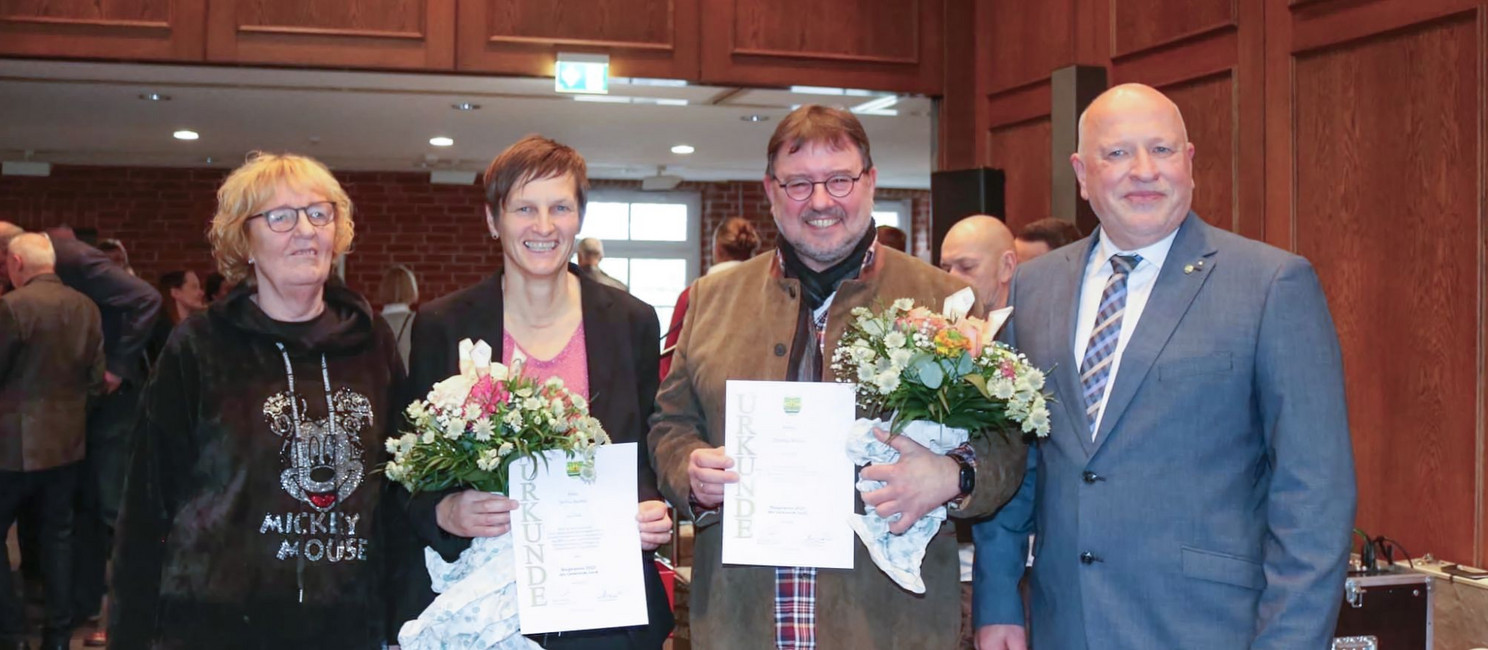 Britta Satzy auf einem Gruppenfoto mit drei weiteren Personen. Sie und eine weitere Person halten ein Dokument und Blumen in den Händen.