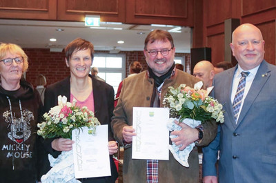 Britta Satzy auf einem Gruppenfoto mit drei weiteren Personen. Sie und eine weitere Person halten ein Dokument und Blumen in den Händen.