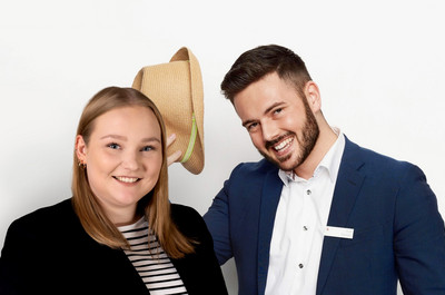 Foto von Monique Kraak und Finn Clausen vor einer weißen Wand. Sie lächeln beide, tragen Anzug und Blazer und Finn hat seinen Hut zum Gruß in der Hand.